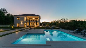 Ein modernes, zweistöckiges Haus mit Swimmingpool und Außenbereich zum Sitzen.