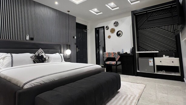 Une chambre moderne avec un grand lit, un bureau, une chaise, un téléviseur et un luminaire fixé au plafond.