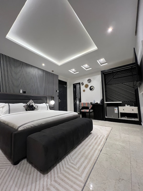Un dormitorio moderno con una cama grande, un escritorio, una silla, un televisor y una lámpara en el techo.