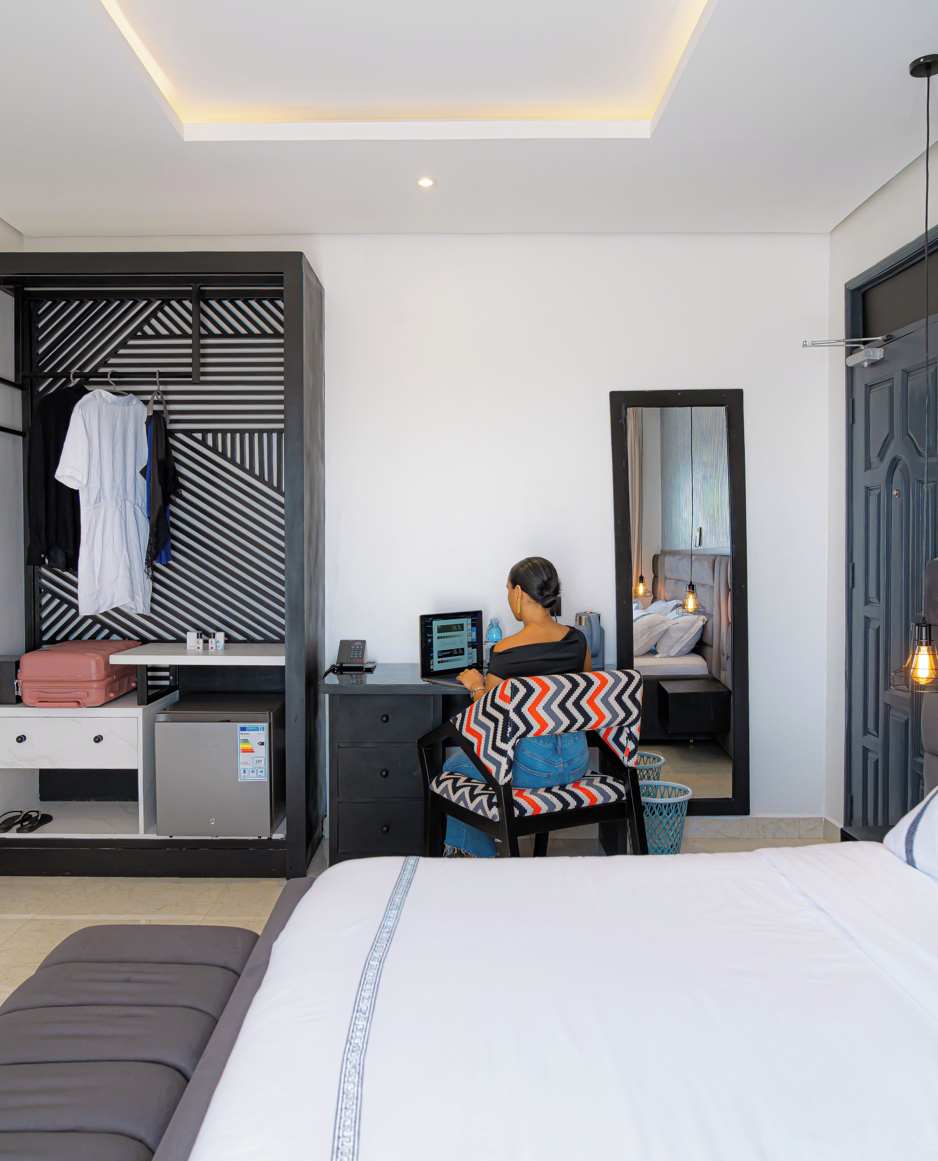Een moderne hotelkamer met een bed, een bureau met een laptop, een kledingkast en een spiegel.