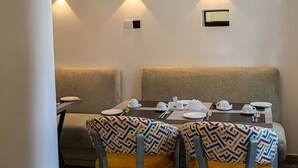 Un coin repas avec une table dressée pour quatre personnes, deux chaises dotées de coussins à motifs et un luminaire suspendu.