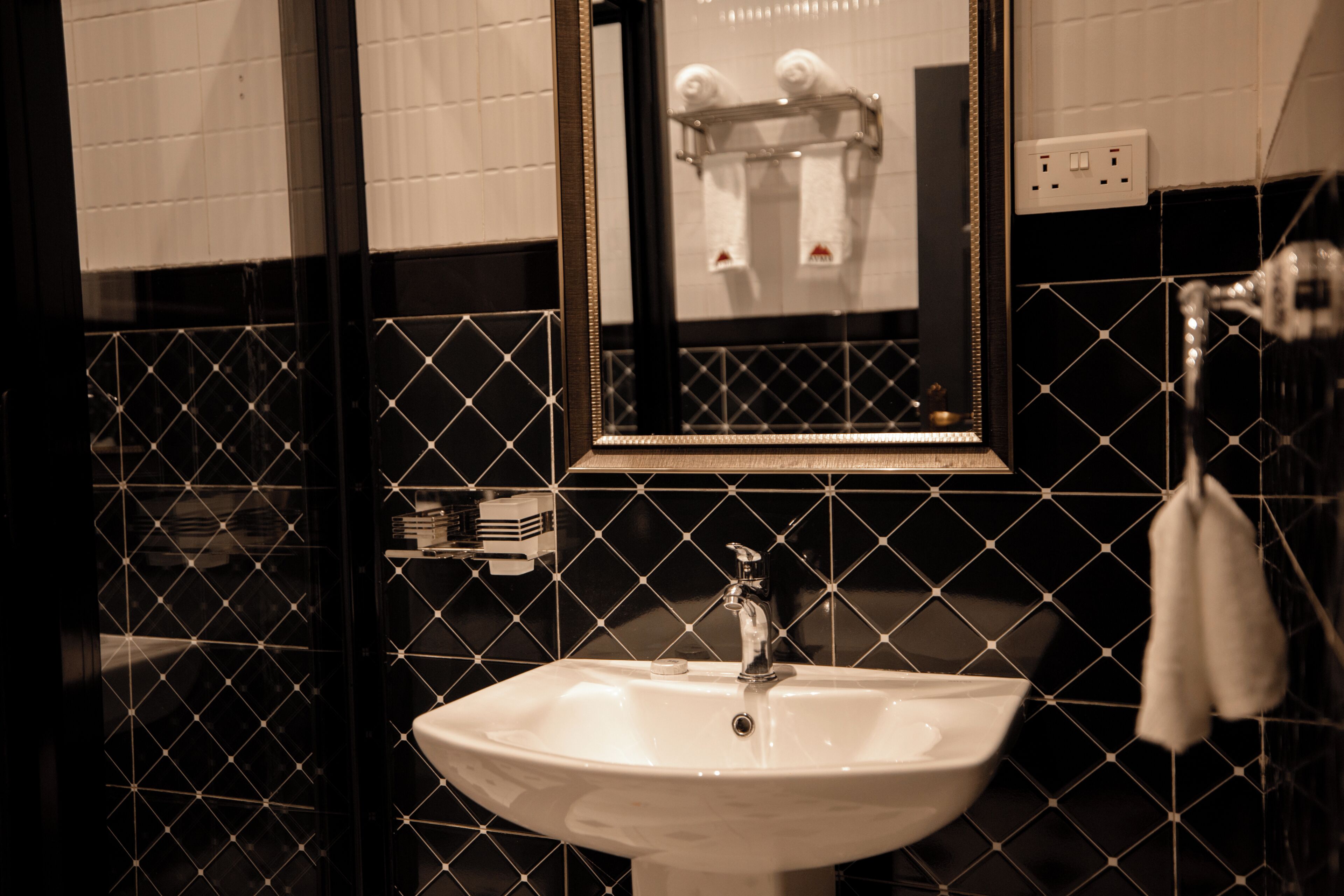 Un baño con un lavabo blanco, paredes revestidas de azulejos negros y un espejo sobre el lavabo.
