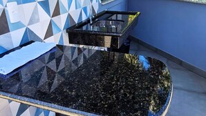En sort bordplade i granit med vask og armatur, bagvæg med blå og hvide geometriske fliser, og en blå væg.