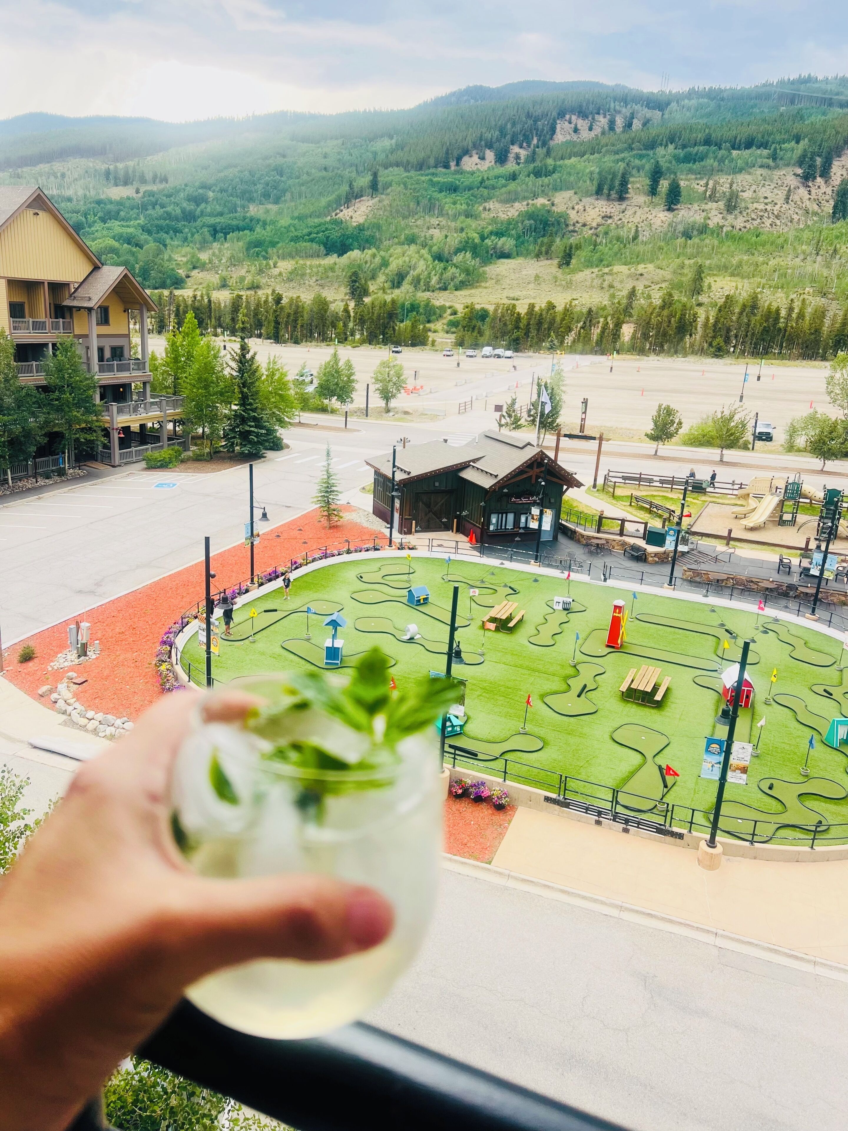 A view of a building with a balcony, a green lawn with a playground, and a mountainous landscape in the background.