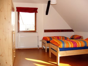 Une chambre à coucher avec deux lits en bois, une fenêtre ornée d’une lambrequin rouge, un radiateur et un plafond en pente.