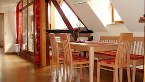 Ein Essbereich mit Holztisch und Stühlen, einer Blumenvase und Blick ins Freie durch große Fenster.