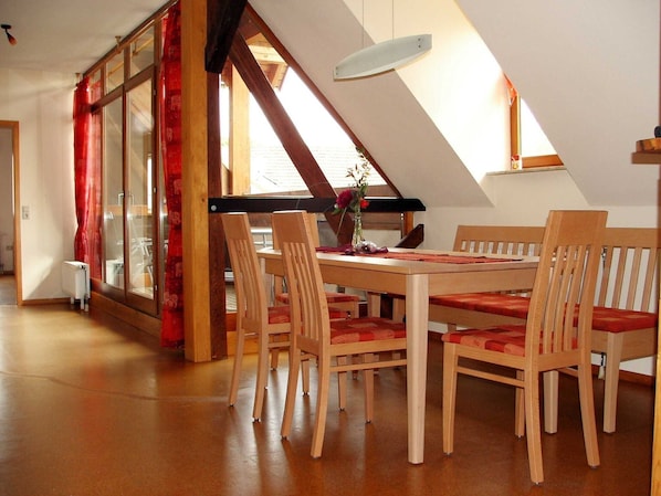 Un coin repas avec une table et des chaises en bois, un vase rempli de fleurs et une vue sur l  ’extérieur grâce à de grandes fenêtres.