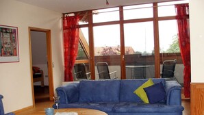 Ein Wohnzimmer mit einem blauen Sofa, einem Holztisch und Blick durch große Fenster.