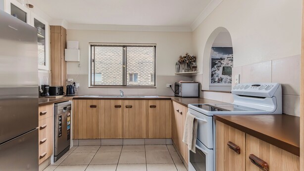A modern kitchen with wooden cabinets, stainless steel appliances, and a large window with a view of a brick building. - Layback on Marine (Kingscliff)