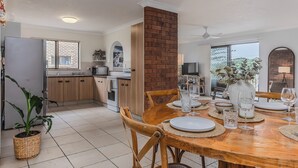 A modern kitchen with wooden cabinets, a brick accent wall, and a dining area with a round wooden table set for six. - Layback on Marine (Kingscliff)