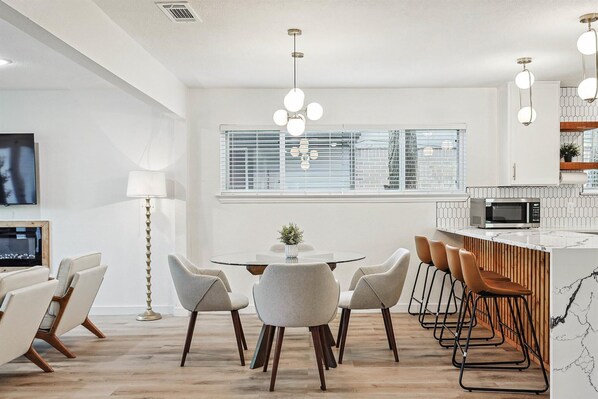 A modern kitchen with a round dining table, bar stools, and a built-in microwave. - Bright Modern Home | 3BR, 2BA, Fenced Backyard (Irving)
