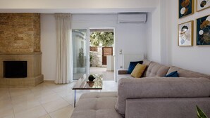 Ein Wohnzimmer mit Kamin, einer Couch, einem Glastisch und Blick durch eine Glastür in einen Außenbereich.