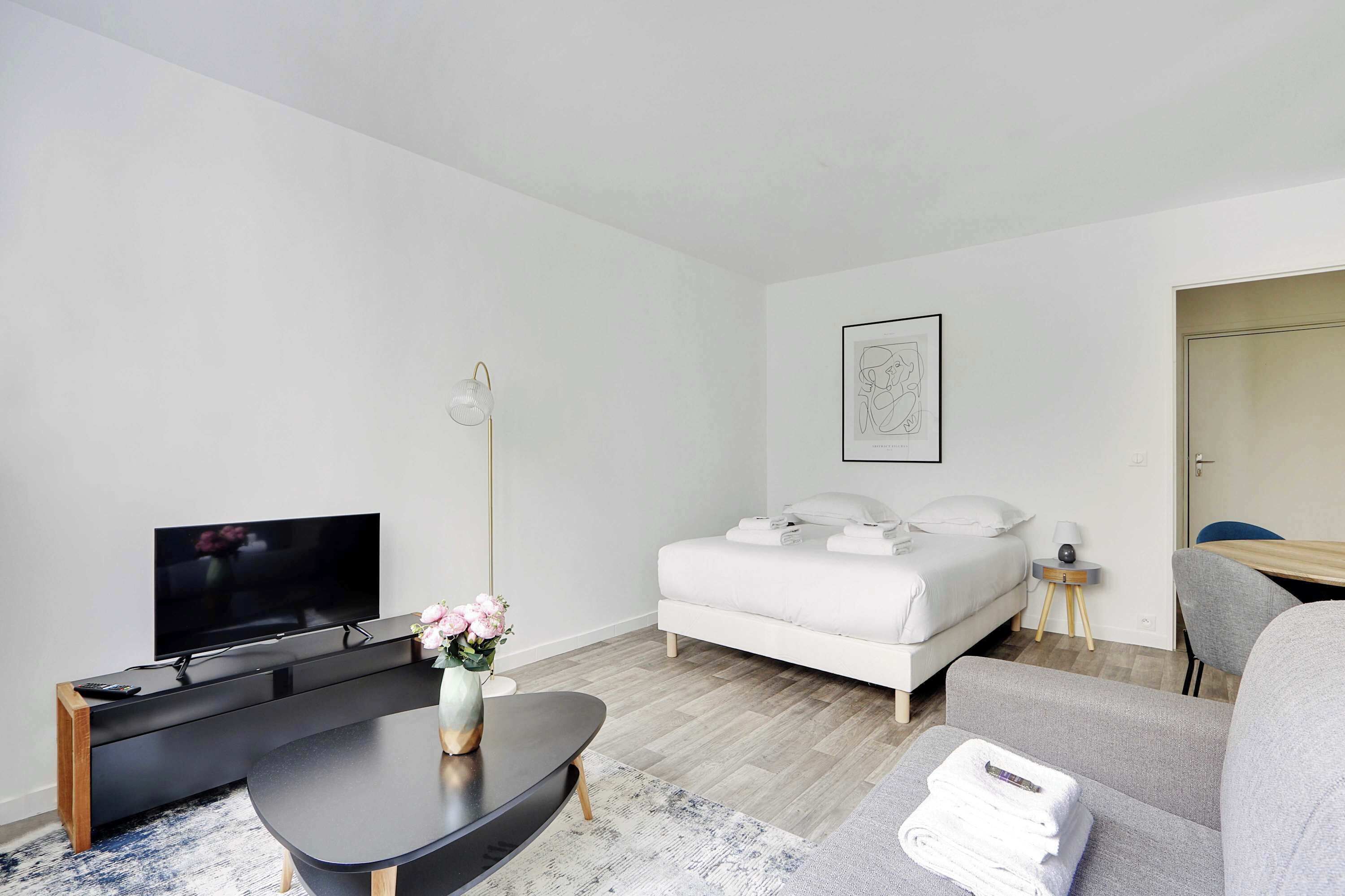 Ein modernes Hotelzimmer mit Flachbildfernseher, einer Couch, einem Bett und einem kleinen Tisch mit Blumenvase.