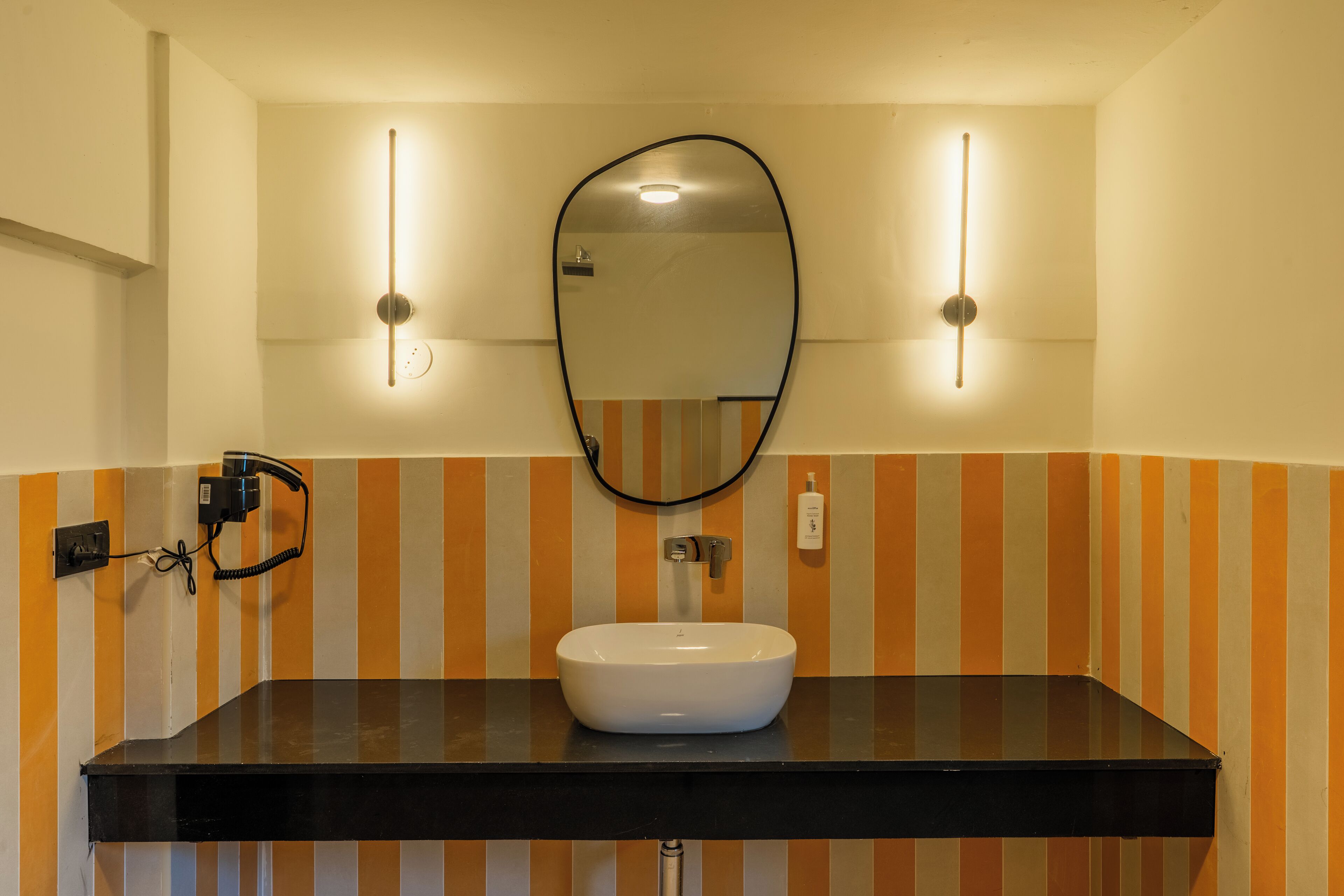 A bathroom with a white sink, black countertop, and striped orange and white walls.