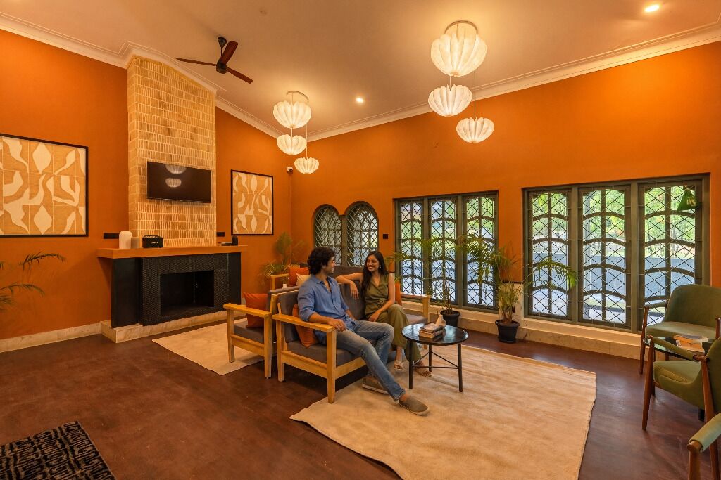 A living room with a fireplace, two sofas, a coffee table, and large windows with green frames.