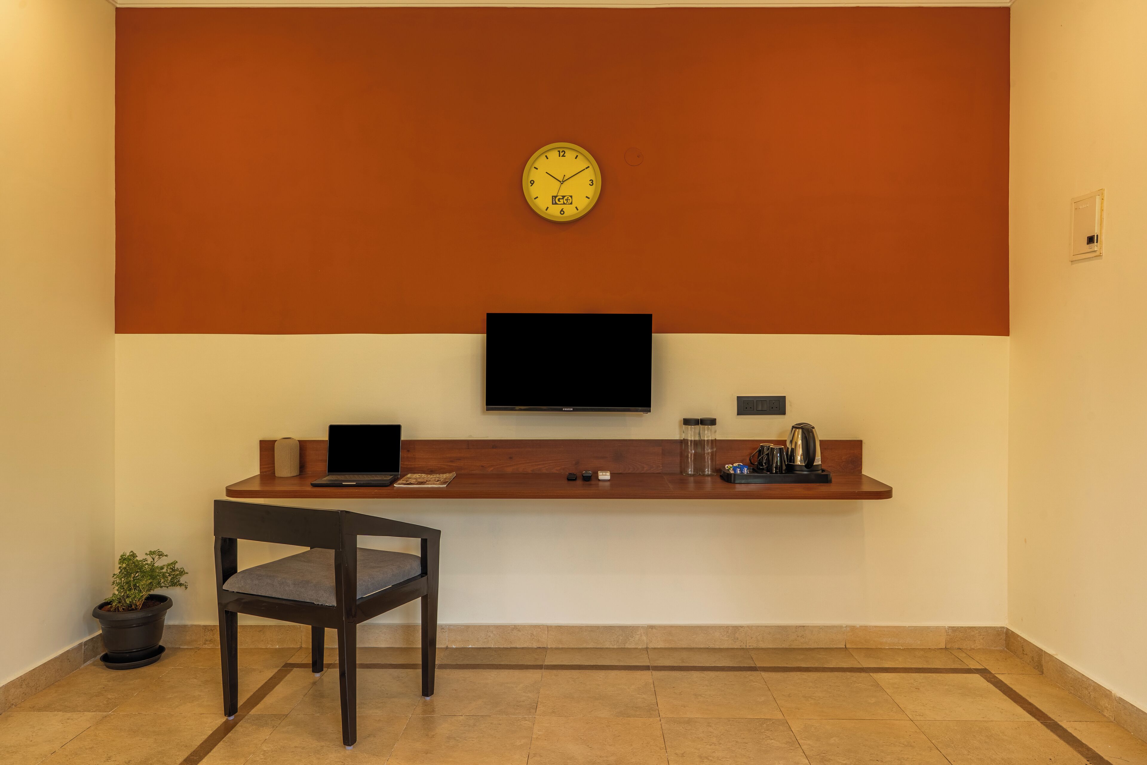 A reception area with a clock, a flat-screen TV, a wooden counter, a chair, and a potted plant.