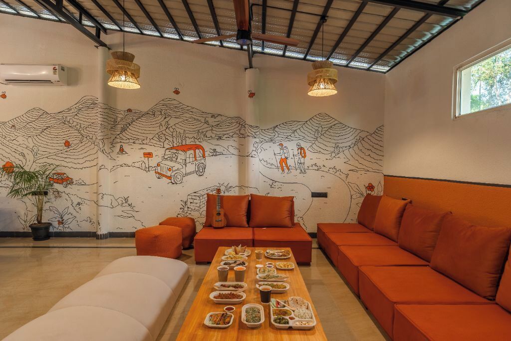A modern living room with a long dining table set with food, orange sofas, and a mural of a mountainous landscape.