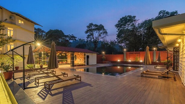 Un espace aménagé au bord de la piscine, avec des chaises longues et des parasols, une petite piscine et un bâtiment doté d’un toit rouge.