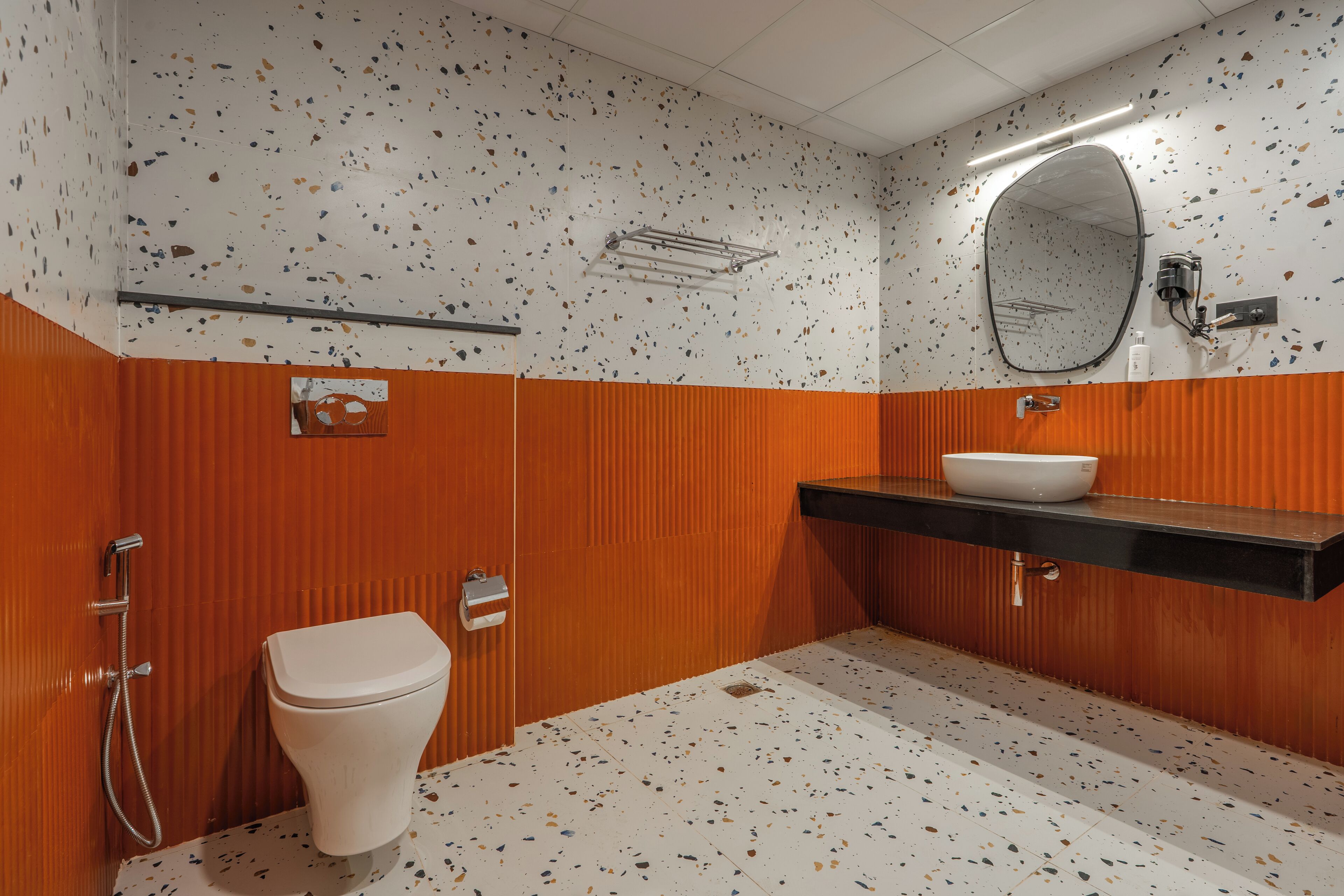 A bathroom with a white toilet, orange walls, a black sink, and a speckled floor.