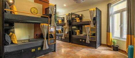 A dormitory room with bunk beds, a clock, and a window with curtains.