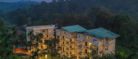 Un hotel de varios pisos con techo verde, rodeado de exuberante vegetación y colinas.