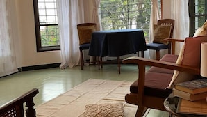 A room with large windows, a table, chairs, and a rug. - Whispering Palms Kodaikanal (Kodaikanal)