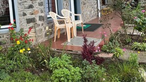 A stone building with a balcony, a small garden with various plants and flowers, and two plastic chairs on the patio. - Whispering Palms Kodaikanal (Kodaikanal)