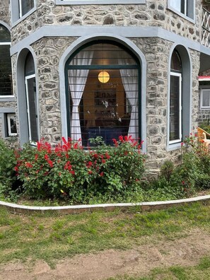 A stone building with a large arched window and a garden with red flowers. - Whispering Palms Kodaikanal (Kodaikanal)