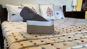 A neatly made bed with a floral-patterned bedspread and pillows, a woven basket on the bed, and a bedside table with a lamp. - Whispering Palms Kodaikanal (Kodaikanal)