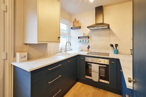 A modern kitchen with dark cabinetry, a white countertop, and stainless steel appliances. - Host & Stay | Daisy Cottage (Masham)