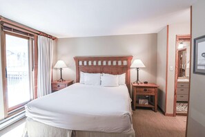 A hotel room with a large bed, two bedside tables with lamps, a wooden headboard, a dresser, and a large window with curtains. - The Plaza 231 | Walk to CBMR Lifts | 2BR Sleeps 6 (Crested Butte)