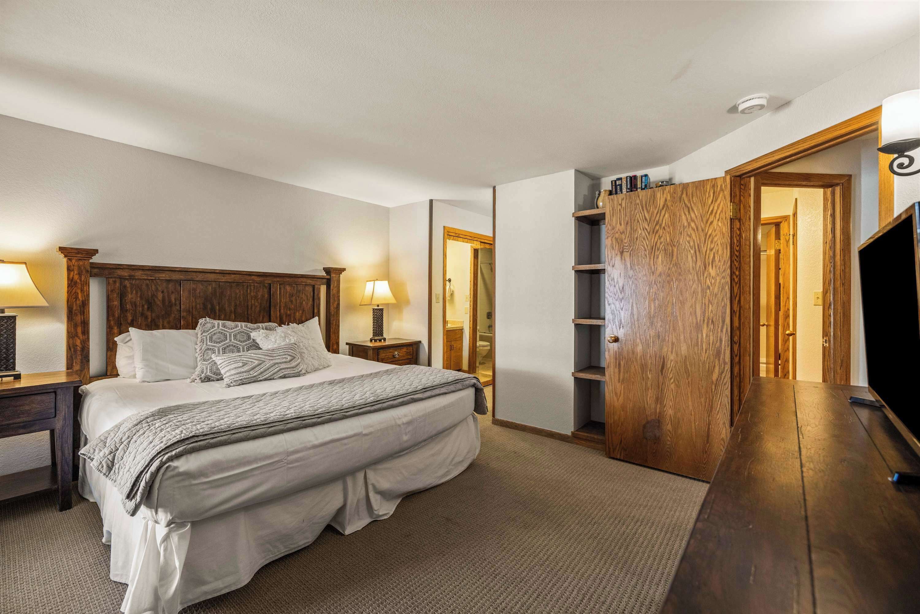 【Bedroom 1 — Primary King】King under wood-beam ceiling — the quiet end of the condo