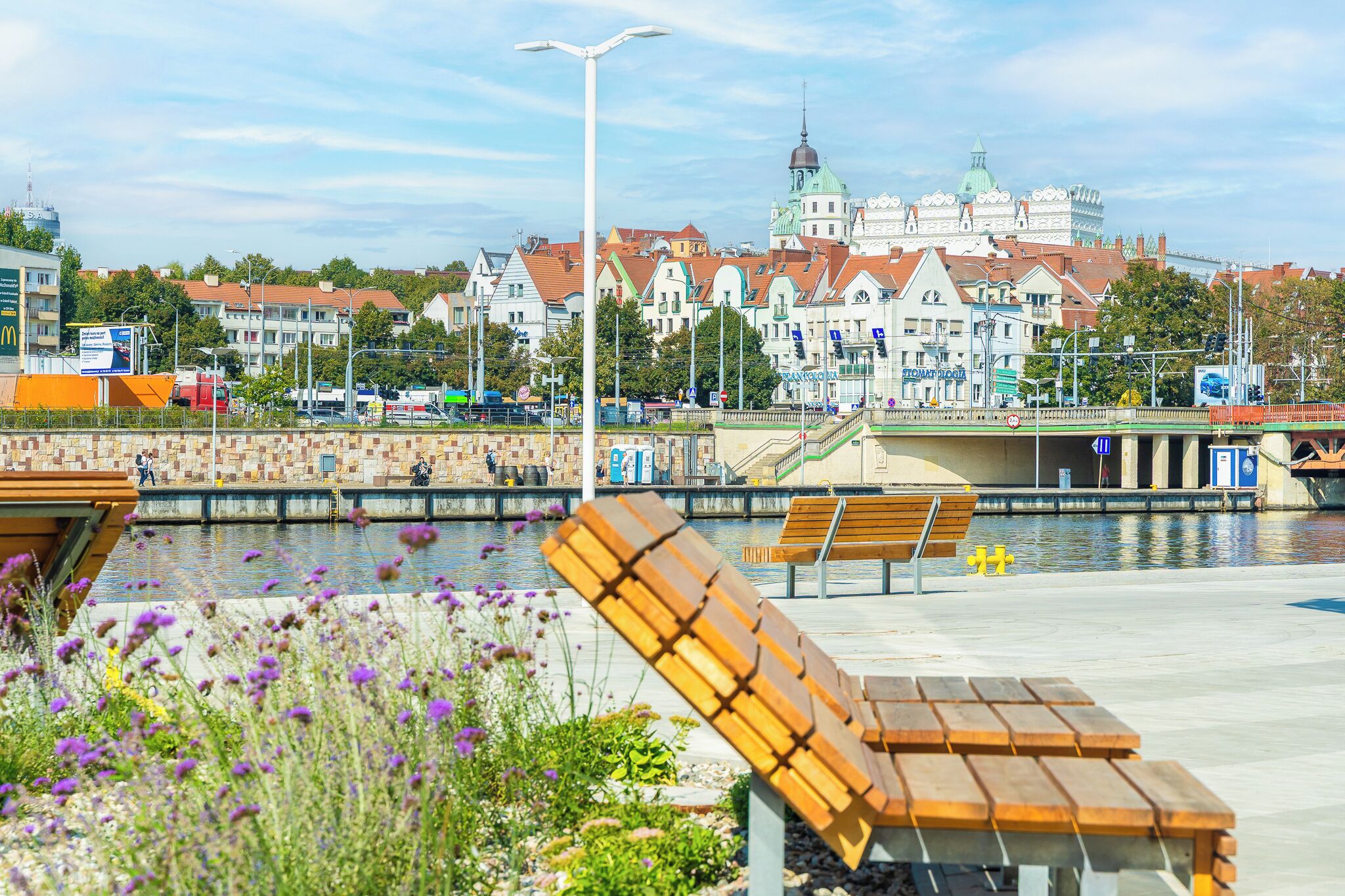 Een waterkantpromenade met banken en een uitzicht op historische gebouwen op de achtergrond.