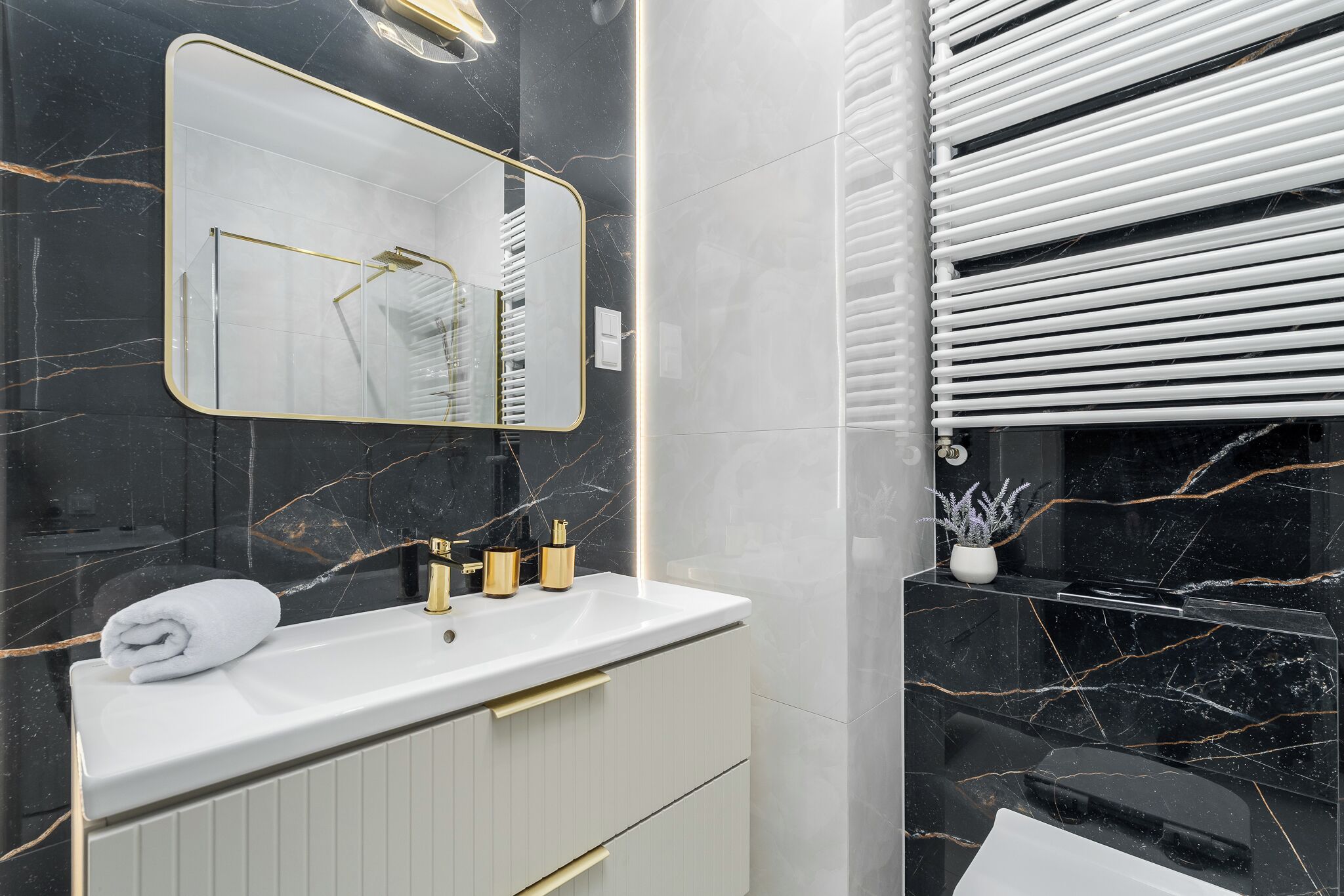 Een moderne badkamer met een witte wastafel, gouden kraanwerk en een marmeren spatwand.