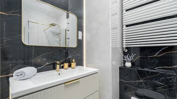 Een moderne badkamer met een witte wastafel, gouden kraanwerk en een marmeren spatwand.