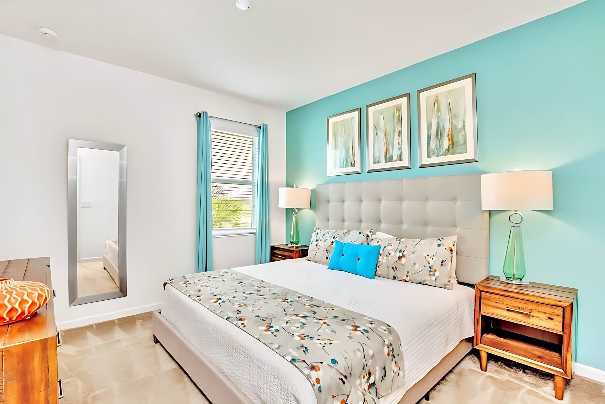 A bedroom with a large bed, two bedside tables, a mirror, and a window with curtains.