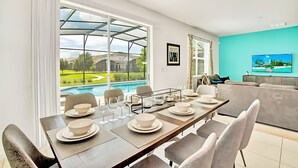 Ein Essbereich mit Blick auf einen Swimmingpool, ein großes Fenster und eine türkisblaue Wand mit einem Fernseher.