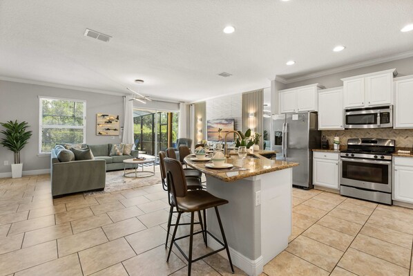 A modern kitchen with a central island, stainless steel appliances, and a dining area with a sofa and chairs. - Upstay Solterra Villa with Private Pool & Hot Tub (Davenport)