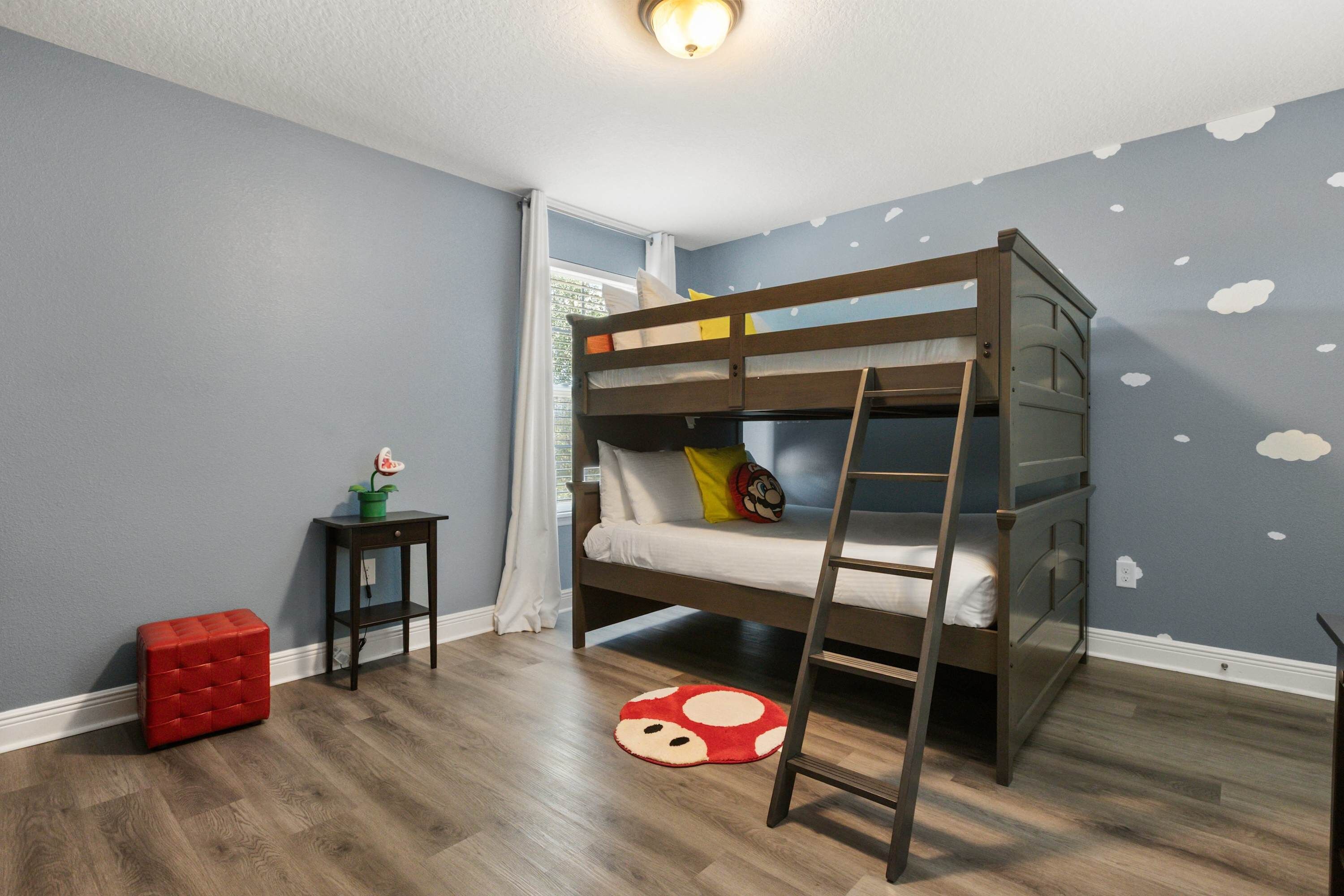 Habitación con literas, una escalera de madera, un reposapiés pequeño rojo y un adhesivo mural con estampado de nubes.
