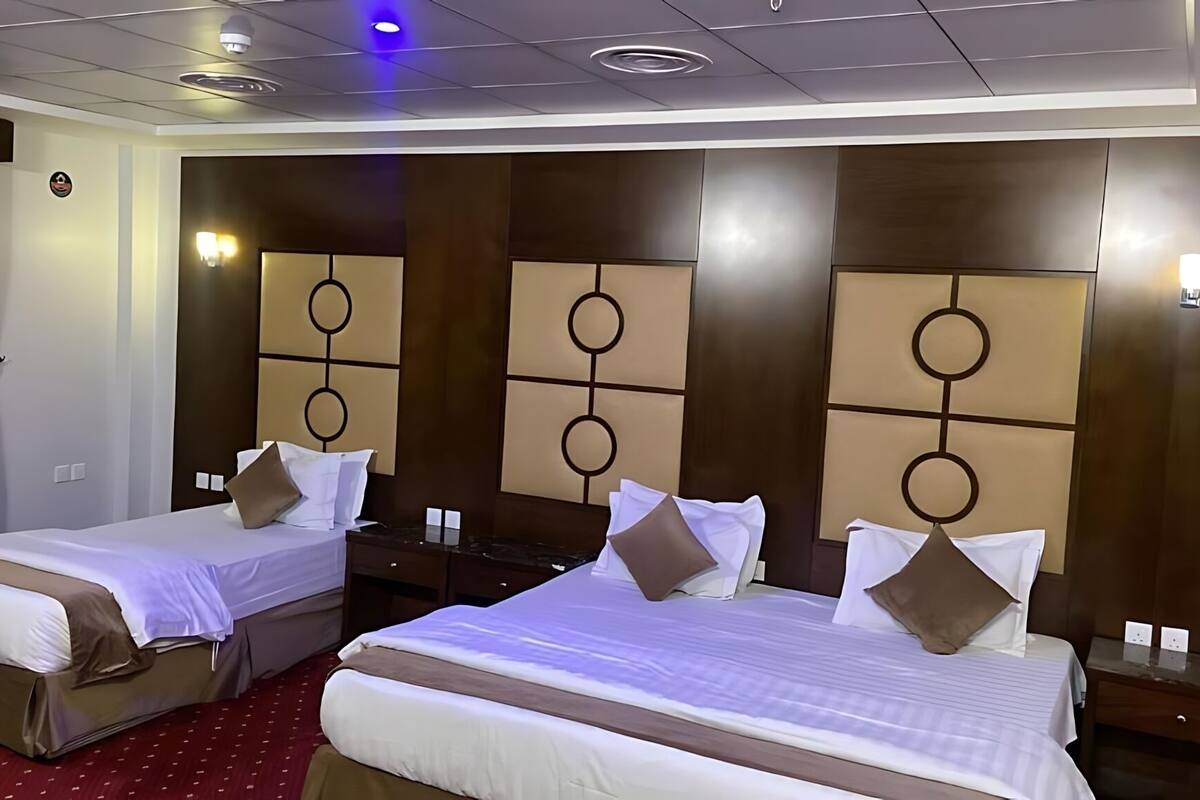 A hotel room with two beds, each with a headboard featuring circular designs. There are bedside tables with lamps, and the room has a red carpet.
