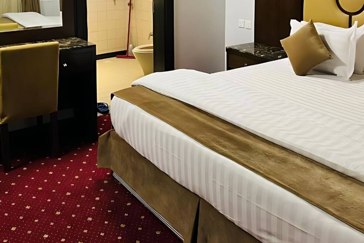A hotel room with a bed, a desk, a mirror, and a door leading to a bathroom.