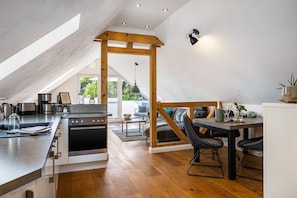 A modern kitchen with a central island, wooden beams, and a dining area with a table and chairs. - Apartment Auf'm Hühnerstall, 60 sqm, 1 Bedroom, Max. 2 Guests (Lennestadt)