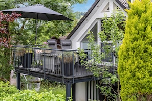 Una zona relax all'aperto con tavola e sedie, un ombrello nero e vista su una casa con balcone.