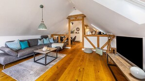 Un espacio habitable tipo loft con techo inclinado, vigas de madera, un sofá, una mesa de centro y un televisor.
