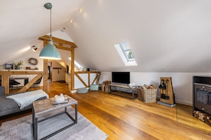 Un living in stile loft con soffitto in legno, zona pranzo, televisione e camino.