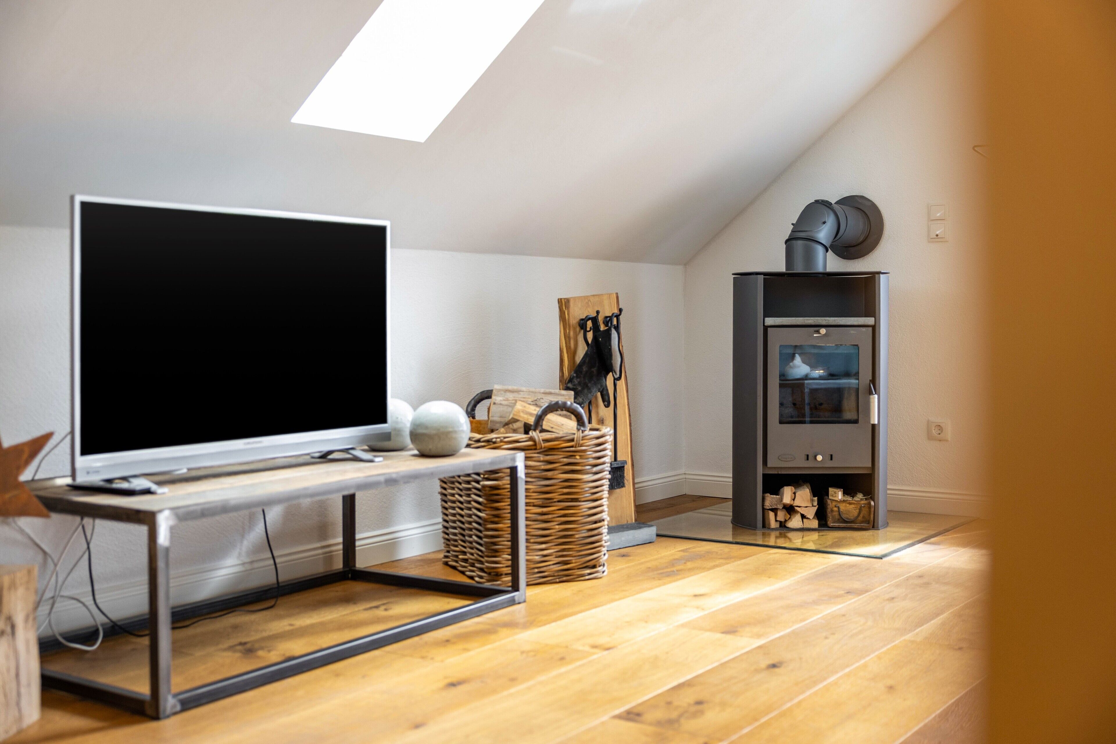 A modern living room with a large flat-screen TV, a wooden floor, a ceiling light, a wall-mounted cabinet, and a fireplace.
