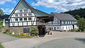 Un edificio tradicional con entramado de madera y fachada de piedra, con un porche cubierto y un patio empedrado.