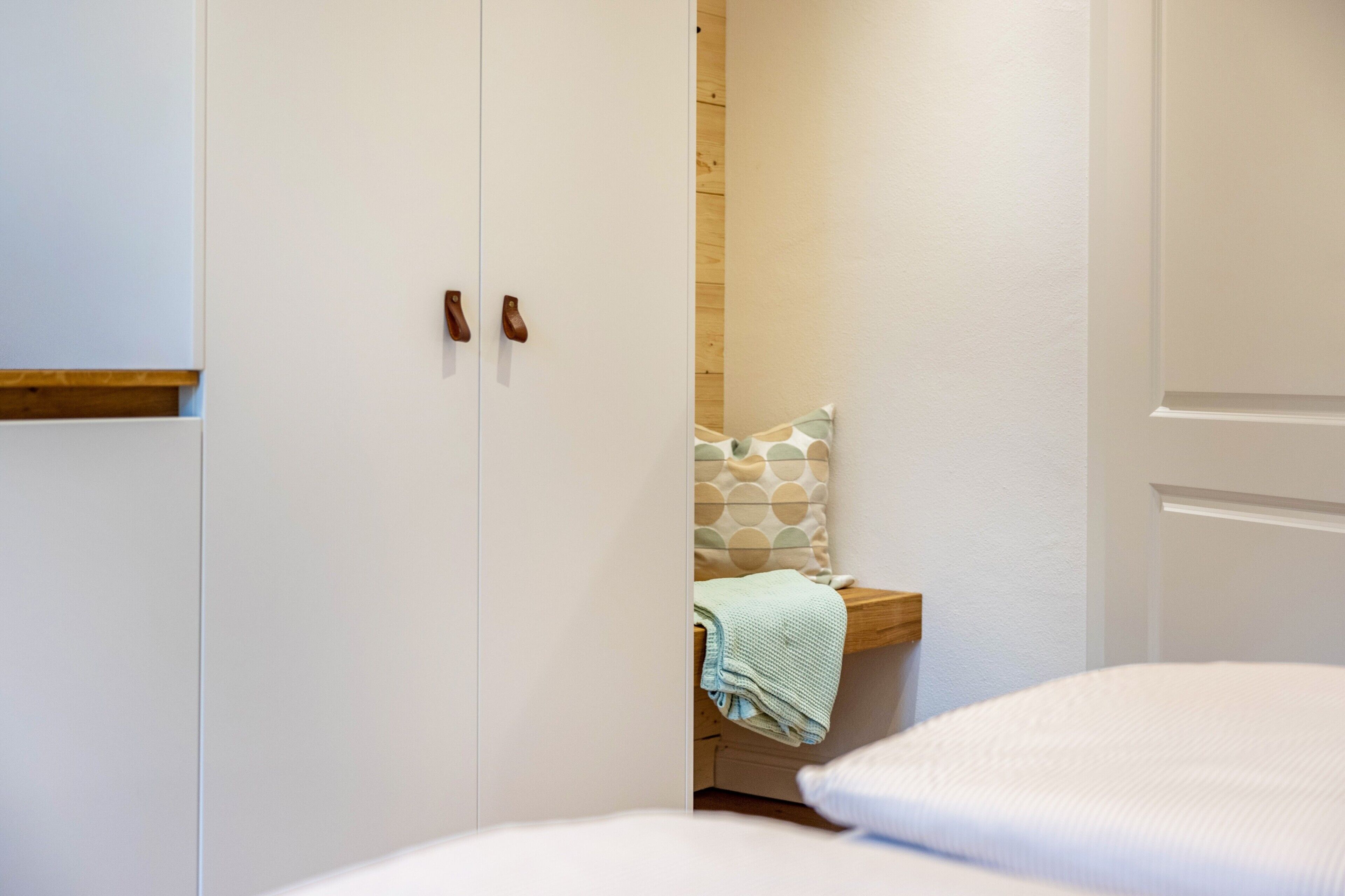 Une chambre à coucher comprenant un lit, un banc en bois, un oreiller et une armoire à deux portes.