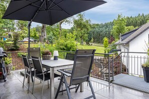 An outdoor patio with a table and chairs, a large umbrella, and a view of a green landscape. - Holiday Apartment 'Auf'm Kornboden', 120 sqm, 2 Bedrooms, Max. 4 Guests (Lennestadt)