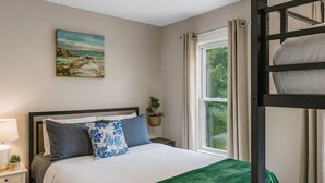 Ein Schlafzimmer mit Etagenbett, Nachttisch mit Lampe, einem Fenster mit Vorhängen und einem Bild an der Wand.